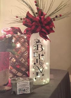 a lighted bottle with the word believe on it next to a christmas tree and presents