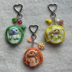 three keychains with different designs on them sitting on a white cloth covered floor