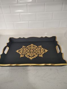 a black and gold tray with an ornate design on the bottom, sitting on a counter