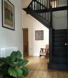 a room with a stair case next to a green plant and a painting on the wall