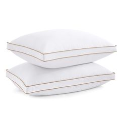 two white pillows stacked on top of each other in front of a white background with gold piping