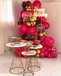 a pink and gold birthday party with balloons on the wall, cake table and chairs