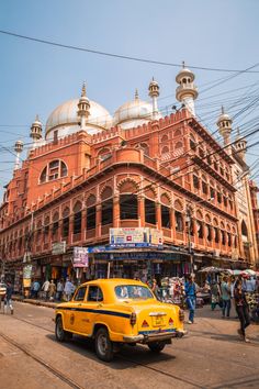 a yellow taxi cab driving down a street next to a tall building with domes on top