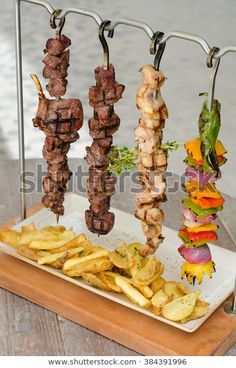 several skewered meats and french fries on a tray