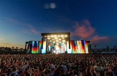 a large group of people sitting in front of a stage with lights on it's sides