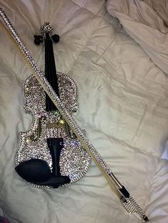 a violin laying on top of a bed covered in white sheets and silver sequins