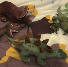 several stuffed dinosaurs are laying on a bed