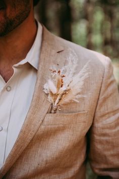 a man wearing a tan suit and white shirt with a feather boutonniere on his lapel