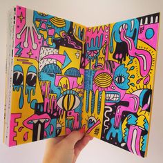 a person holding up an open book with colorful designs on it's front cover