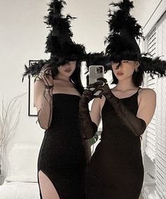 two women in black dresses are taking a selfie with their cell phones and hats