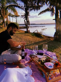 a man sitting at a picnic table with two wine glasses on it and another person holding a bottle