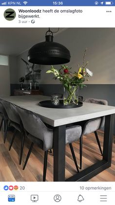 a dining room table with chairs and flowers in vase on the center piece, next to a black pendant light