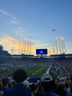 a football stadium filled with lots of people watching the sun go down and fireworks in the sky