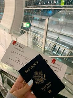 a person holding up a passport and boarding pass in front of an escalator