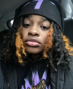 a woman with curly hair wearing a beanie and looking at the camera while sitting in a car