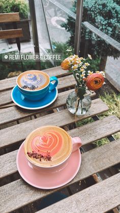 two cups of coffee sitting on top of a wooden table next to flowers and vases