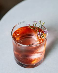 a glass filled with liquid and flowers on top of a white countertop next to a table