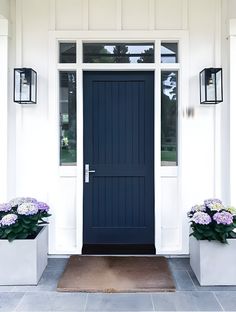 two white planters with purple flowers in front of a blue and white door on a house