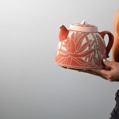 a person holding a red and white teapot with designs on the outside, in front of a gray background