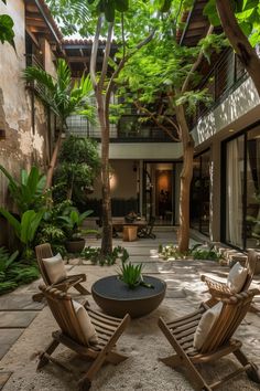 two lawn chairs sitting on top of a stone floor next to trees and plants in front of a building