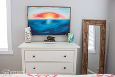 a bedroom with a dresser, mirror and painting on the wall