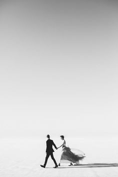 a man and woman walking in the desert holding hands with each other, while wearing long veils