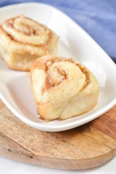 two cinnamon rolls on a white plate with a wooden cutting board in the foreground