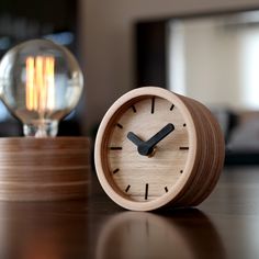 a small wooden clock sitting on top of a table next to a lightbulb