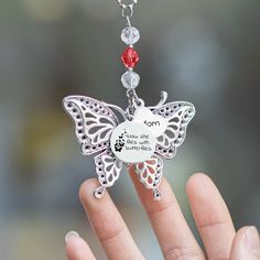 a hand holding a silver charm with a red beaded butterfly on it's back