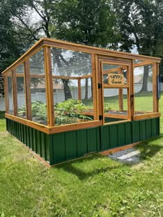 a small green house sitting in the middle of a grass covered field with plants growing inside