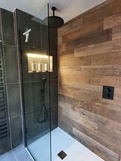 a bathroom with a glass shower door and wooden wall behind the shower head is illuminated by lights