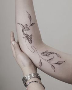 two hands holding each other with tattoos on their arm and wrist, one has a fish in it