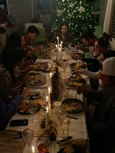 a group of people sitting around a dinner table eating food and drinking wine at christmas time