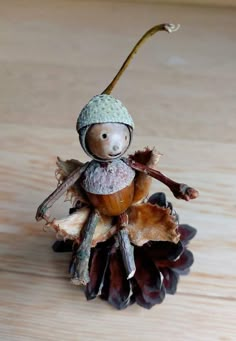 a small figurine sitting on top of a pine cone with leaves and acorns