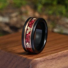 a wedding ring with red and gold inlays sits on top of a wooden surface