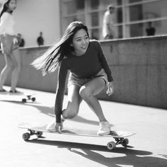 a woman riding a skateboard down a sidewalk next to another person on a skateboard