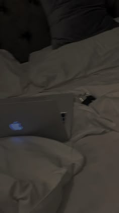 an apple laptop sitting on top of a white bed covered in sheets and pillows,