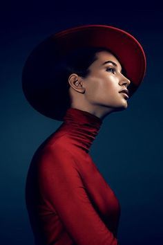 a woman in a red dress and hat with her head turned to the side looking up