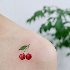 two cherries on the back of a woman's left shoulder, with green leaves