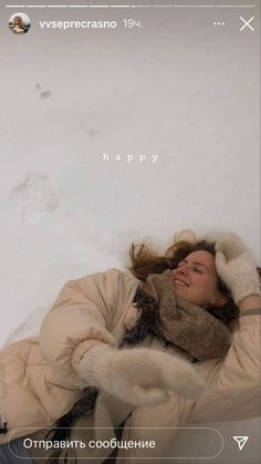 a woman is laying in the snow with her arms around her head and holding a cat