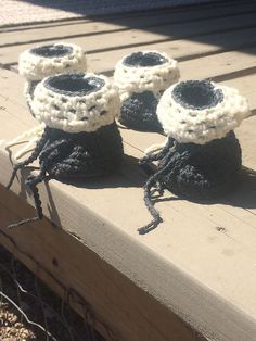 three crocheted black and white baby booties sitting on top of a wooden bench