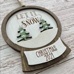 a wooden ornament with two trees on it and the words let it snow