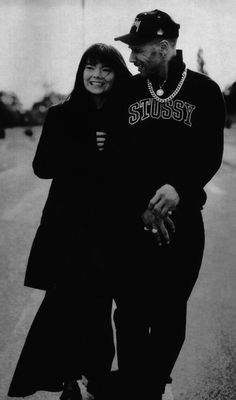 a black and white photo of a man and woman walking down the street, both wearing hoodies