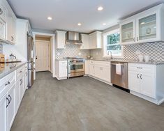 an empty kitchen with white cabinets and silver appliances in the center, along with marble counter tops