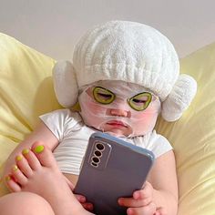 a baby in a white hat is holding a cell phone and looking at it's screen