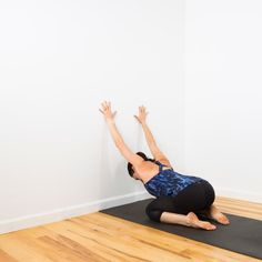 a woman is doing yoga on a mat in front of a white wall and hardwood floor