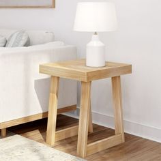 a small wooden table with a white lamp on it next to a couch and coffee table