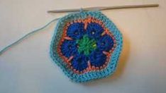 a blue crocheted pot holder with a needle in the middle and an orange, green, and blue design on it