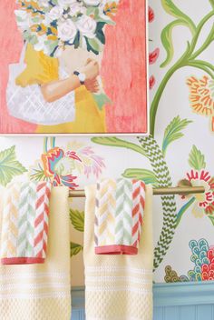 two towels are hanging on a rack in front of a wall with flowers and a painting