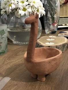 a clay giraffe sitting on top of a wooden table next to a vase filled with flowers